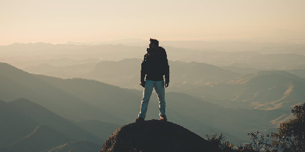 A man standing on a mountain overlooking a sunset lanscape